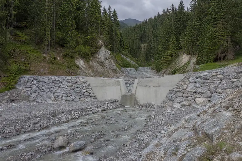 Une plage de dépôt en graviers, fermée par un barrage en béton à fente, retient les pierres d'un torrent de montagne.
